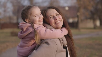 mother is circling child in her arms, cheerful kid with mom, happy family, children's dream of flying, baby smiles and laughs, parent in arms of little funny girl, beloved daughter playground day off.
