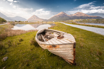 Old rowboat on grass near peaceful lake and hills in rural Scotland countryside at sunset