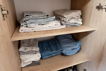 Bed linen, sheets and pillowcases and towels neatly stacked in closet in bedroom