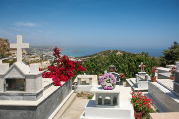 A peaceful cemetery on a hillside in Kos Island, Greece, featuring marble crosses, vibrant flower...