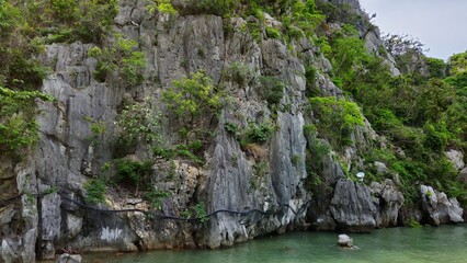Limestone cliffs and lush greenery, with a small sandy beach and calm emerald sea of Thiên Cung cave, Ha Long Bay, Vietnam.