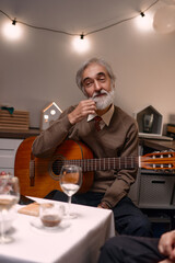 A man with a guitar enjoys a warm and intimate dinner with friends in a cozy home setting.
