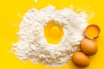 Making dough concept. Pile of flour and eggs on yellow background top view
