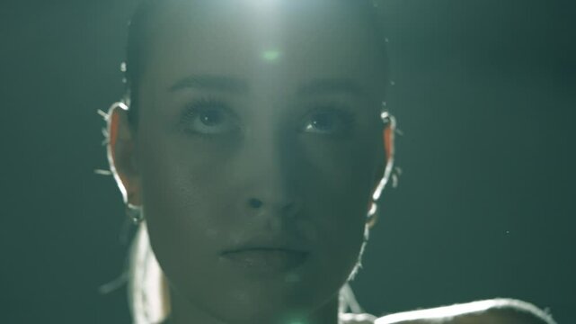 Twarz kobiety w filmowym swietle w czasie treningu na rowerze stacjonarnym w ciemnej sali siłowni 