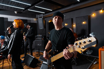 Professional musicians practicing together in studio space, playing musical instruments, and singing vocals. Highlighting creativity, and musical performance in a rehearsing and creative environment.