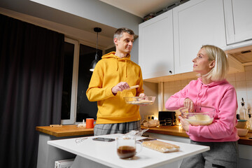 A man and woman wearing comfortable attire work together in a warm home kitchen, preparing food. The environment is cozy with bright lighting and modern appliances that enhance the atmosphere.