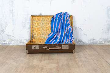 Vintage retro suitcase, the suitcase is open and there is a scarf in it, stand on a stool. The background is a white wall. The concept of retro travel and retro design.