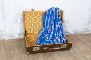 Vintage retro suitcase, the suitcase is open and there is a scarf in it, stand on a stool. The background is a white wall. The concept of retro travel and retro design.