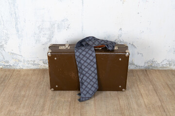 Vintage retro suitcase, the suitcase and there is a scarf on it, stand on a stool. The background is a white wall. The concept of retro travel and retro design.
