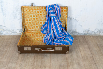 Vintage retro suitcase, the suitcase is open and there is a scarf in it, stand on a stool. The background is a white wall. The concept of retro travel and retro design.