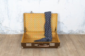 Vintage retro suitcase, the suitcase is open and there is a scarf in it, stand on a stool. The background is a white wall. The concept of retro travel and retro design.