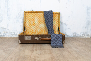 Vintage retro suitcase, the suitcase is open and there is a scarf in it, stand on a stool. The background is a white wall. The concept of retro travel and retro design.