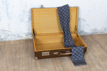 Vintage retro suitcase, the suitcase is open and there is a scarf in it, stand on a stool. The background is a white wall. The concept of retro travel and retro design.