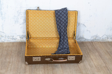 Vintage retro suitcase, the suitcase is open and there is a scarf in it, stand on a stool. The background is a white wall. The concept of retro travel and retro design.