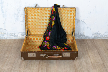 Vintage retro suitcase, the suitcase is open and there is a scarf in it, stand on a stool. The background is a white wall. The concept of retro travel and retro design.