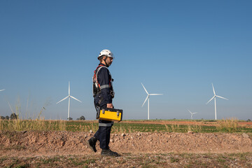 Engineer wearing uniform inspection and survey work in wind turbine farms rotation to generate electricity energy. Maintenance engineer working in wind turbine farm at sunset.