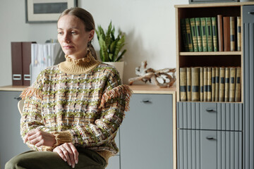 Portrait of woman sitting with eyes closed during therapy session, hands resting on lap, bookshelf...
