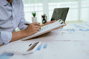 Asian businessman working at desk analyzing financial reports, charts and data using laptop to plan...