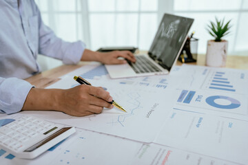 Asian businessman working at desk analyzing financial reports, charts and data using laptop to plan...