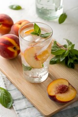 Refreshing glass of water infused with peach slices and basil on a wooden board next to fresh peaches