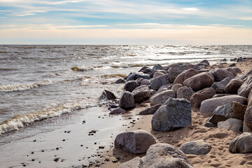 Sunlit round stones and boulders at water's edge on Gulf of Finland beach, beautifully backlit by...