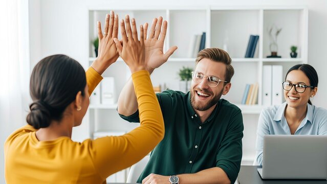 Business team celebrating success at work with high fives and smiles in a bright modern office. Happy coworkers achieving goals together.