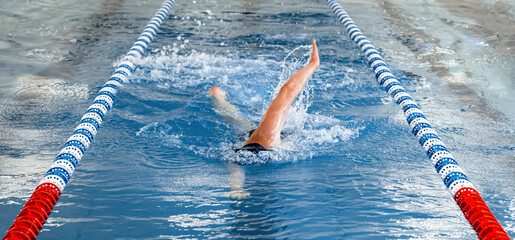 Swimmer performing the backstroke in a competition pool with lane markers visible