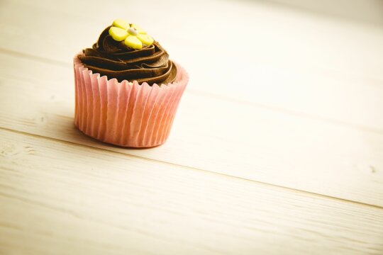 Naklejki Cupcake is resting on pale wooden table in flat design, with chocolate swirl and yellow flower