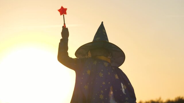 boy in a hat conjures magic wand at sunset, halluin, believe in children's magic, kid plays in the glare of the sun, child's carnival costume for holiday, an astranom festive outfit, childhood dream.
