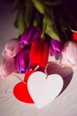 Colorful tulip bouquet is being shown in flat design on pale wooden surface with heart tags