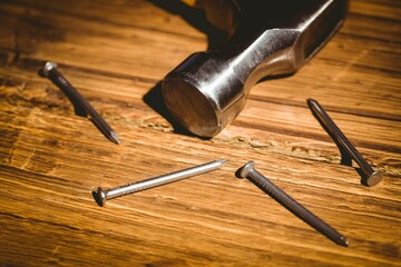 Flat design is showing metallic hammer head resting on warm wood surface with scattered steel nails