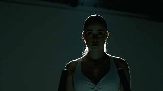 młoda kobieta poprawia włosy i zaczyna trening na rowerku stacjonarnym w ciemnym filmowym pomieszczeniu 