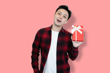 A young Asian man, wearing a red plaid shirt over a white t-shirt, is holding a red gift box