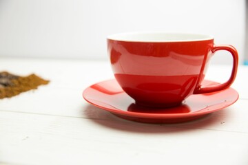 Flat design is showing red ceramic cup and saucer resting on wooden tabletop with scattered grounds
