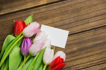 Multicolored tulip bouquet is being shown in flat design on plank tabletop with blank white card