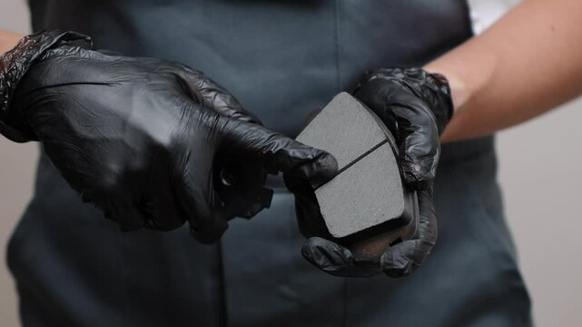 Auto mechanic in black gloves holds two brake pads in hands and touches rough surface with his fingers, close-up. Concept of service, repair of brake system of car, auto service