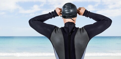 Male swimmer adjusting swimming cap while standing at beach