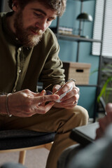 Man holding eyeglasses while listening attentively during therapy session, sitting across from...