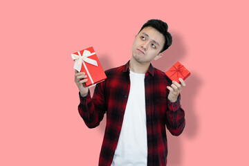 A young Asian man in a red plaid shirt and white t-shirt holds two red gift boxes, His facial...