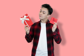 A young Asian man in a red plaid shirt and white t-shirt holds two red gift boxes, His facial...