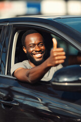 Smiling young African man with a beard giving a thumbs up from the driver's seat of a black car. Bright daylight and urban background.