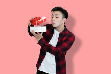 A young Asian man wearing a red plaid shirt over a white t-shirt is holding and looking into an...
