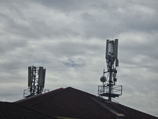 Cell towers with antennas and equipment installed on a rooftop under a cloudy sky. Ideal for...