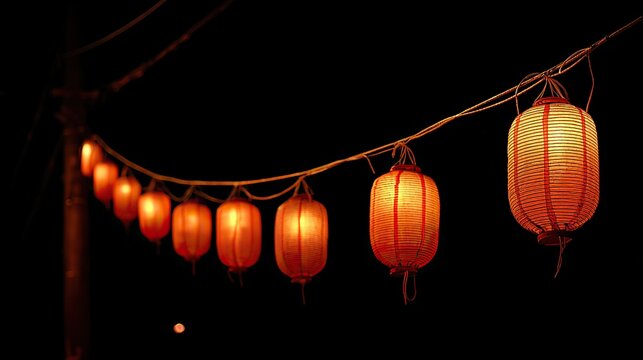 Traditional Japanese paper lanterns hanging on ropes at night, glowing lights symbolizing summer festival celebrations and cultural ambiance - Powered by Adobe