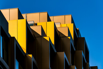 Zigzagging yellow balconies with bold sunlight and deep shadows against a vivid blue sky