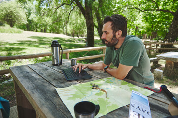 Man Uses Laptop While Planning Outdoor Camping Trip with Map and Compass