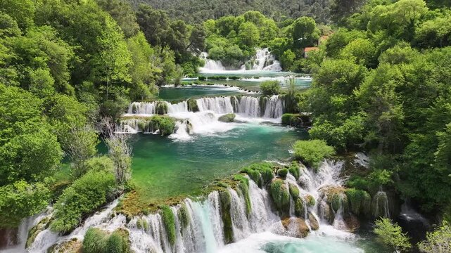 Drone view of waterfalls in Krka National Park flowing between thick forests and moss-covered rocks. Calm, powerful water stream in a protected natural setting.