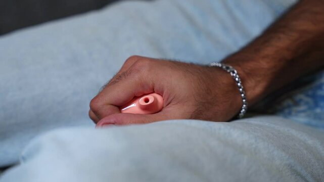 Detailed shot of hand holding peach-colored vape with bracelet, set against denim&mdash;ideal for lifestyle, habits, or wellness themes.