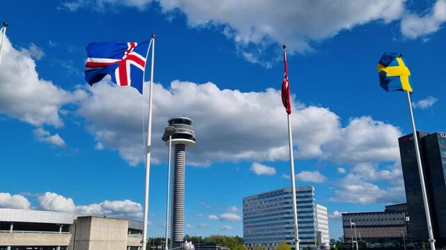 The European Union and various Scandinavian flags sway gently in the wind at Stockholm&rsquo;s Arlanda Airport, with a clear blue sky framing the airport hotel and control tower