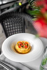 Elegant gourmet ravioli topped with red caviar and fresh herbs, plated on white ceramic, served outdoors with a sophisticated dining background.